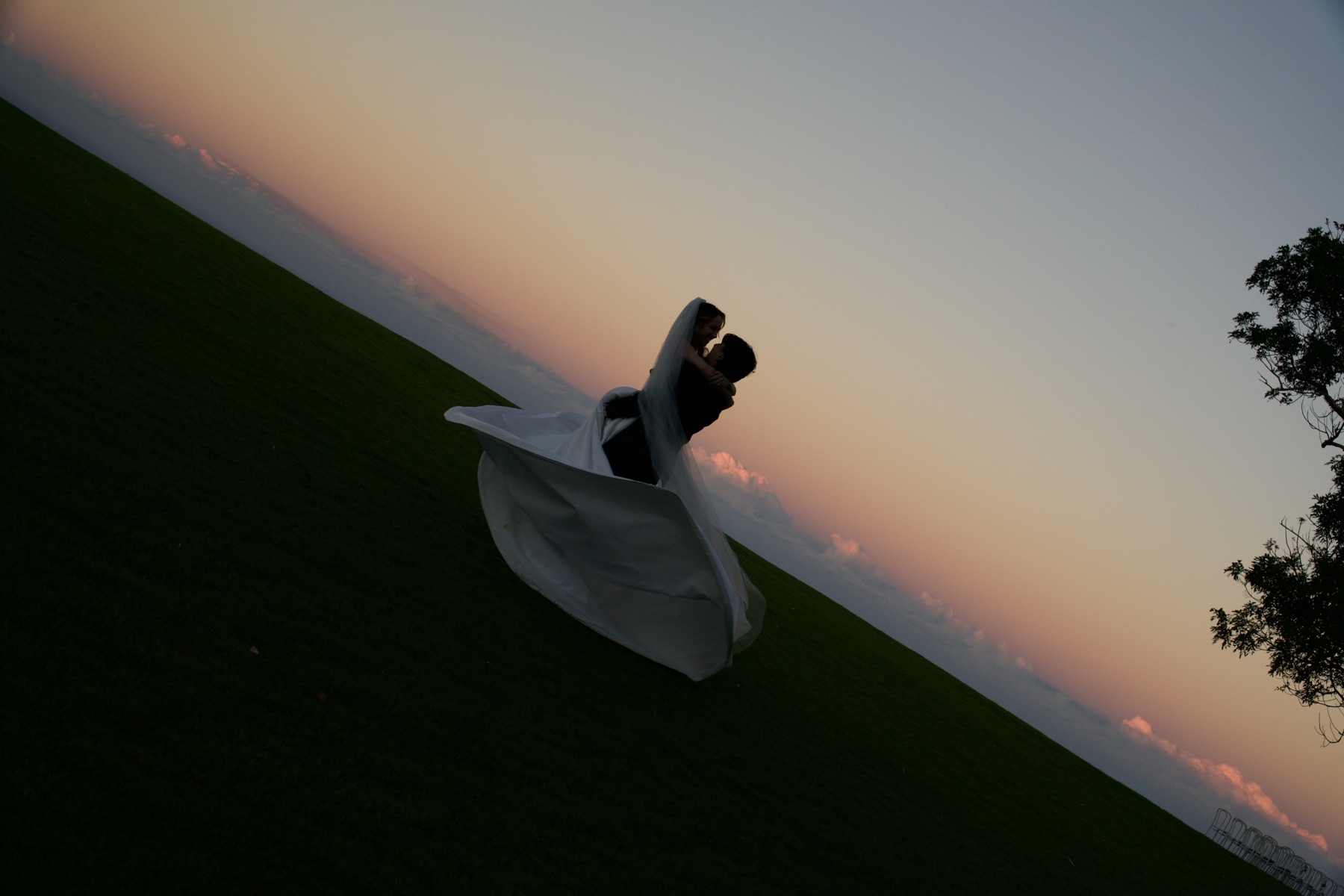 A couple silhouetted on a hilltop as the sky turns pink behind them